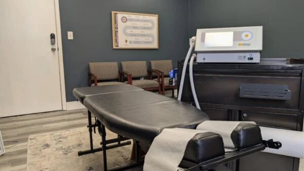 A treatment room featuring a black padded therapy table alongside a SoftWave therapy machine sitting on a dark cabinet.