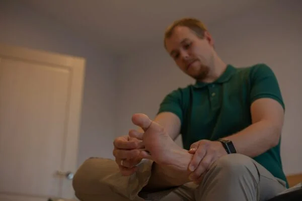 A man sitting cross-legged and rubbing his foot, attempting to stimulate sensation and relieve neuropathy symptoms.