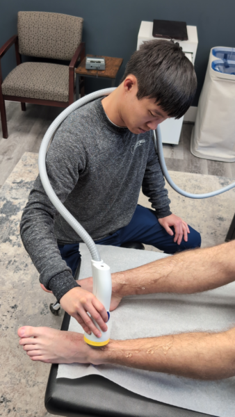 Male healthcare provider using a SoftWave Therapy wand on a patient's lower leg and ankle during a treatment session in a medical office.
