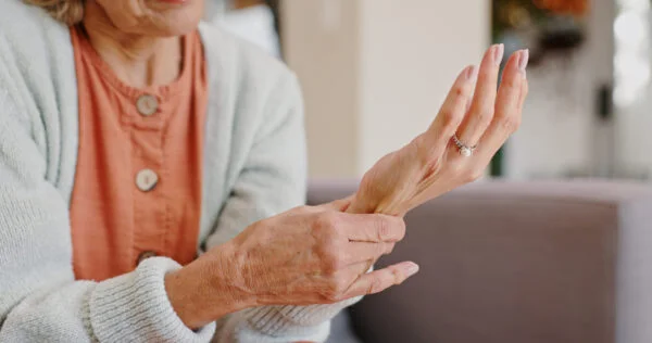 Close-up of an elderly woman holding her stiff, painful wrist and fingers, representing targeted SoftWave therapy treatment for arthritis joint pain.