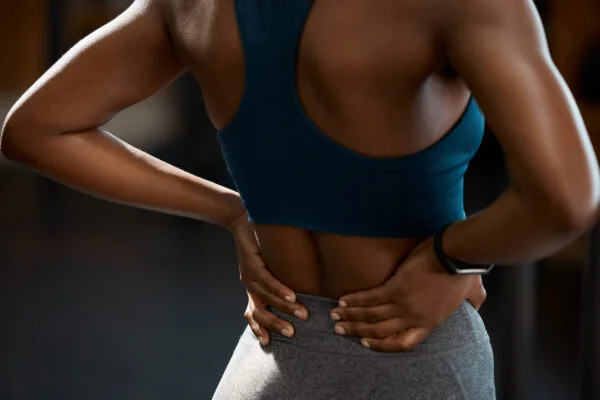 Rear view of a fit woman holding her aching lower back during or after a workout, representing targeted SoftWave therapy for chronic back pain.