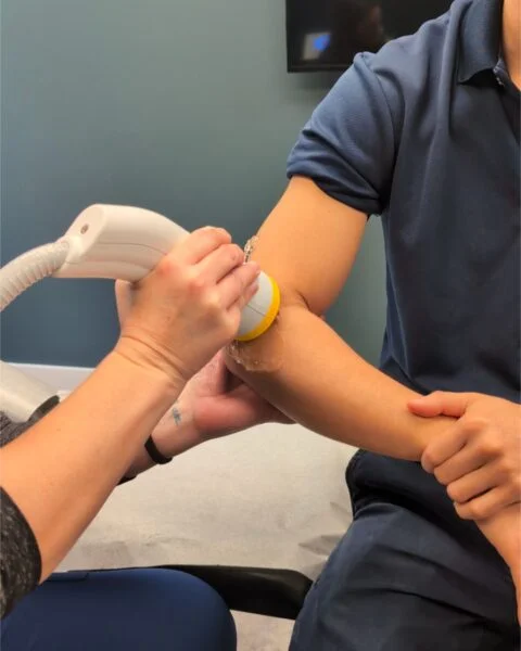 Clinician applying a SoftWave therapy device to a patient's elbow with ultrasound gel, addressing various joint and tendon conditions treated by SoftWave therapy.