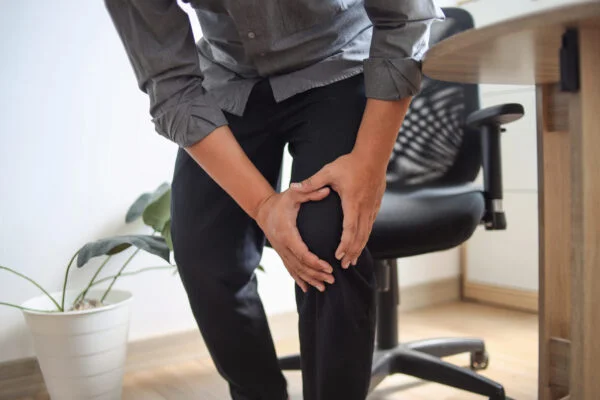 Man gripping his aching knee in discomfort, highlighting SoftWave therapy for knee pain relief.