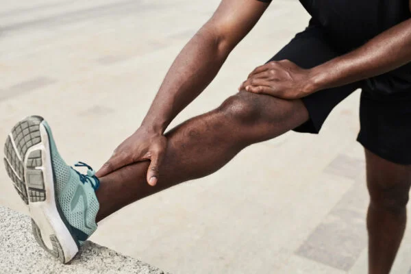 Athlete stretching an extended leg and holding his calf and ankle in discomfort, representing targeted SoftWave therapy treatment for chronic leg pain.