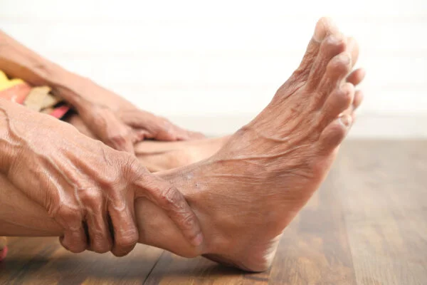 Close-up of hands gripping an aching foot and ankle, representing non-invasive SoftWave therapy treatment for peripheral neuropathy and nerve pain.