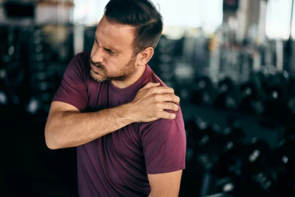 Man wincing in discomfort while gripping his shoulder after a workout, representing targeted SoftWave therapy for chronic shoulder pain.